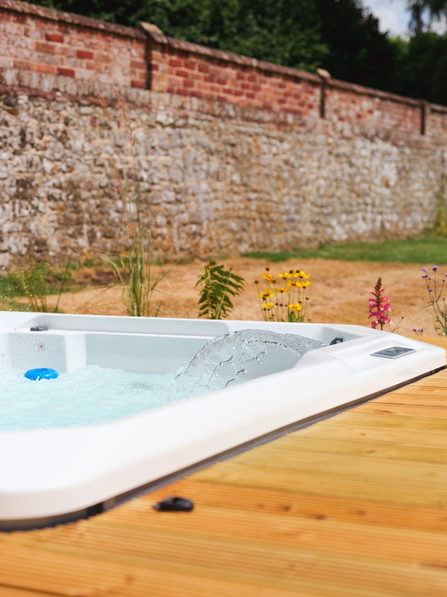 Ein Whirlpool auf einer Holzdielen-Terrasse, im Hintergrund eine Steinmauer.