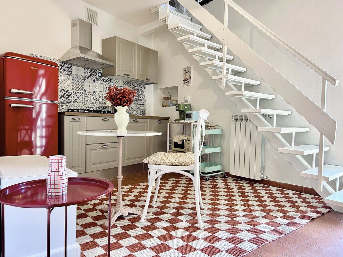 Una cocina con un refrigerador rojo, una silla blanca, una mesa redonda pequeña y un piso con diseño.