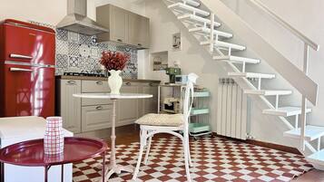 Una cocina con un refrigerador rojo, una silla blanca, una mesa redonda pequeña y un piso con diseño.