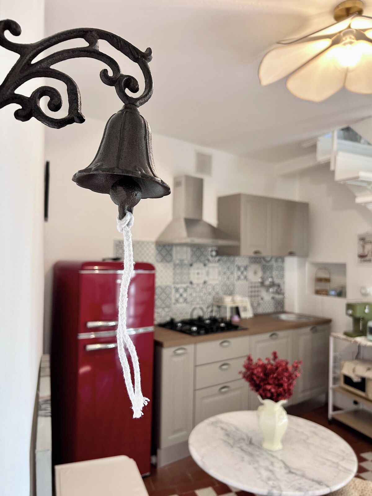 Een keuken met een rode koelkast, een marmeren tafel met een vaas, en een hangklok.
