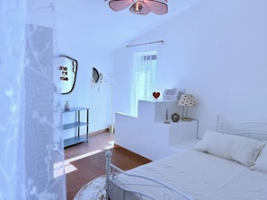 Een slaapkamer met een bed, nachtkastje, raam en wandplank.