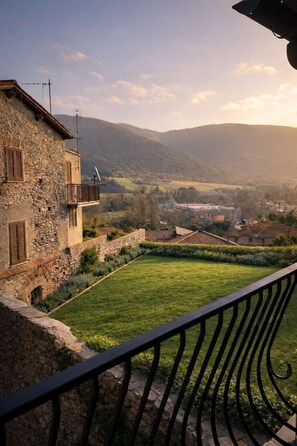 A stone building with a balcony overlooking a grassy area and distant hills.