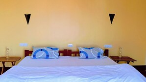 Un lit recouvert d’une couvre-lit à motifs bleus et blancs, deux tables de chevet avec des lampes, un luminaire suspendu et une prise électrique murale.