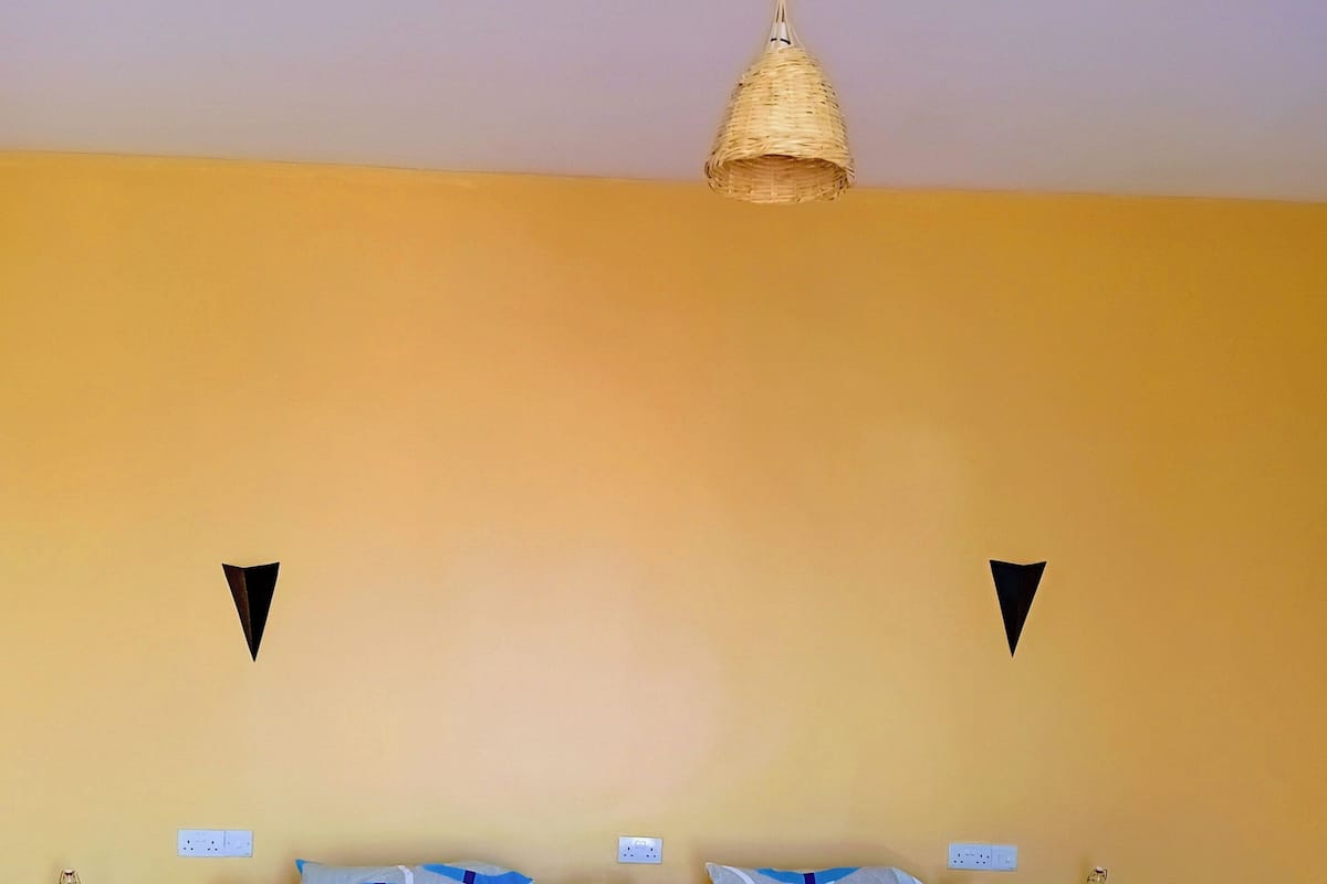 Una cama con una colcha azul y blanca estampada, dos mesitas de noche con lámparas, una lámpara colgante y un enchufe de pared.