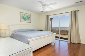 Ein Schlafzimmer mit Bett, Nachttisch, Lampe, Deckenventilator und einem Balkon mit Vorhängen.