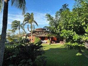 A traditional building with a tiled roof, surrounded by lush greenery and palm trees. - Ideal house for groups in Búzios | 2 houses + pool + staff + sports court + games room (Armação dos Búzios)