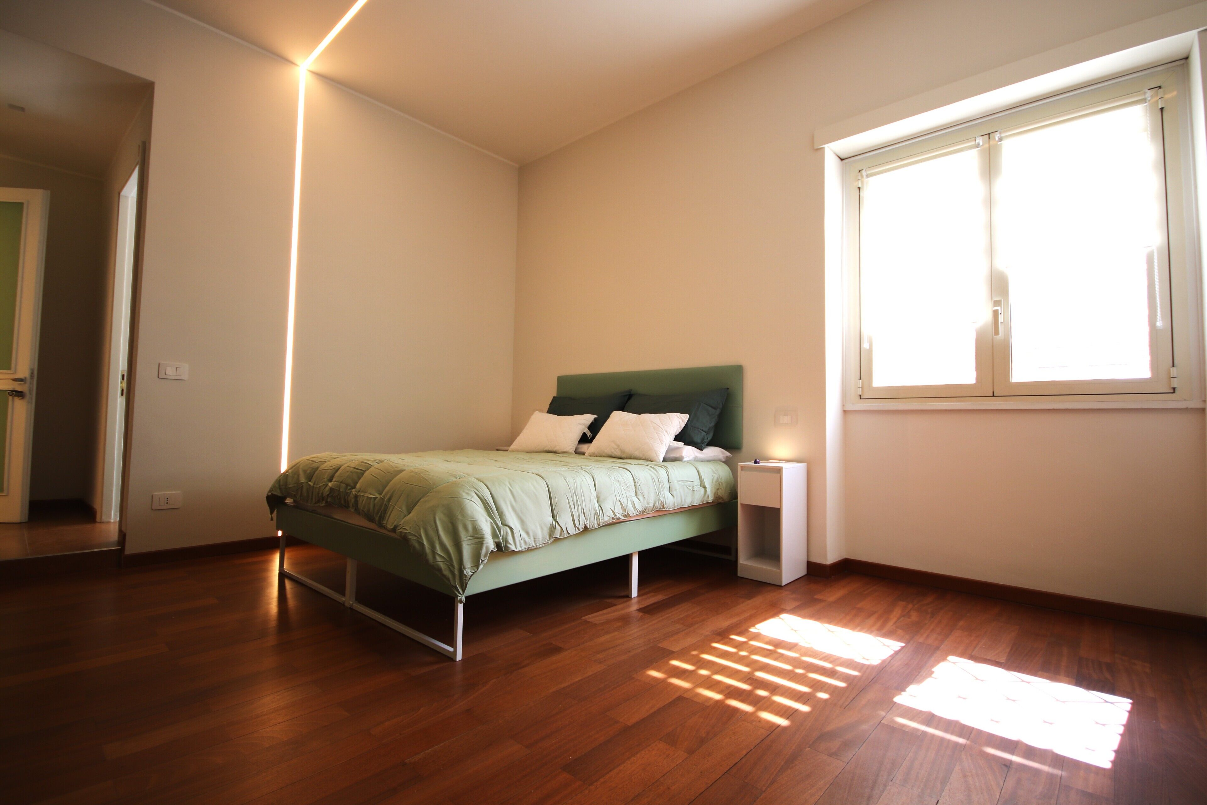 Un dormitorio con cama, mesita de noche y ventana.