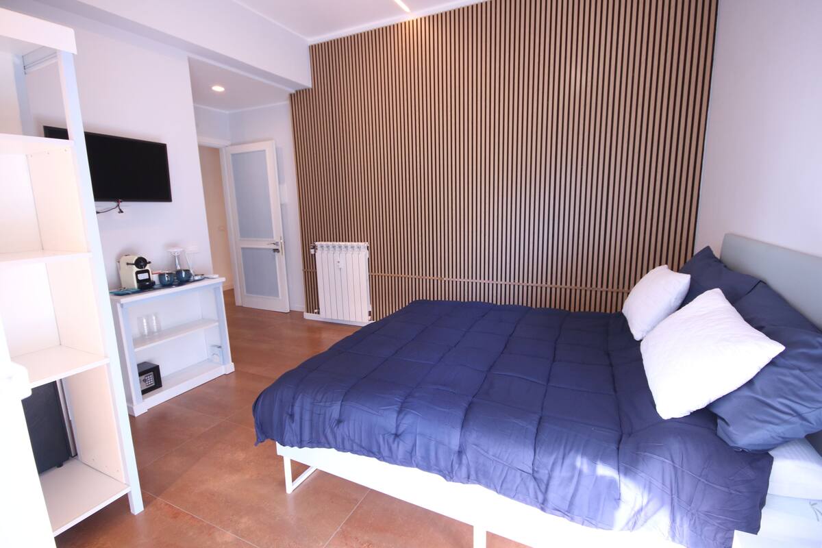 Un dormitorio con una cama, un televisor montado en la pared, un armario blanco y un radiador.