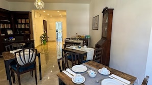 A dining area with a wooden table set for four, surrounded by chairs, a chandelier, and a bookshelf.