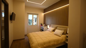 A modern bedroom with a bed, bedside tables, a TV, and a window.