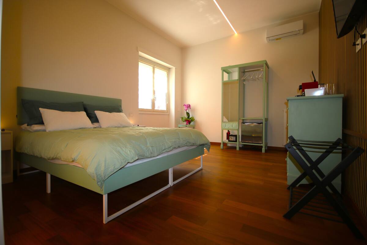 Un dormitorio con cama, ventana, espejo, radiador y armario.