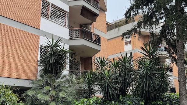 A multi-story building with balconies, a stone pathway, and lush greenery.