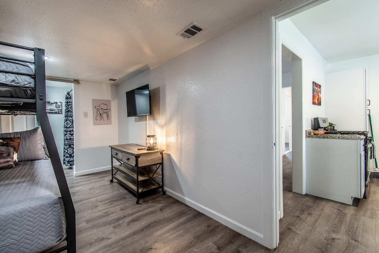 A compact living space with a bunk bed, a desk with a lamp, a television, and a kitchenette.