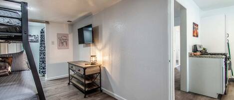A compact living space with a bunk bed, a desk with a lamp, a television, and a kitchenette.