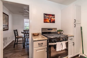 A kitchen with a stove, oven, and cabinets, a dining area with chairs, and a painting on the wall. - Sleeps 18 - Seaside Serenity Dual Dwellings for Family & Friends (Corpus Christi)