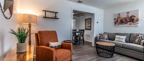 A living room with a sofa, armchair, round coffee table, and a dining area with chairs and a table.