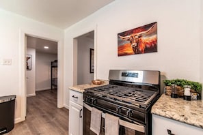 A kitchen with a stainless steel stove, a granite countertop, and a painting of a bull on the wall. - Sleeps 18 - Seaside Serenity Dual Dwellings for Family & Friends (Corpus Christi)