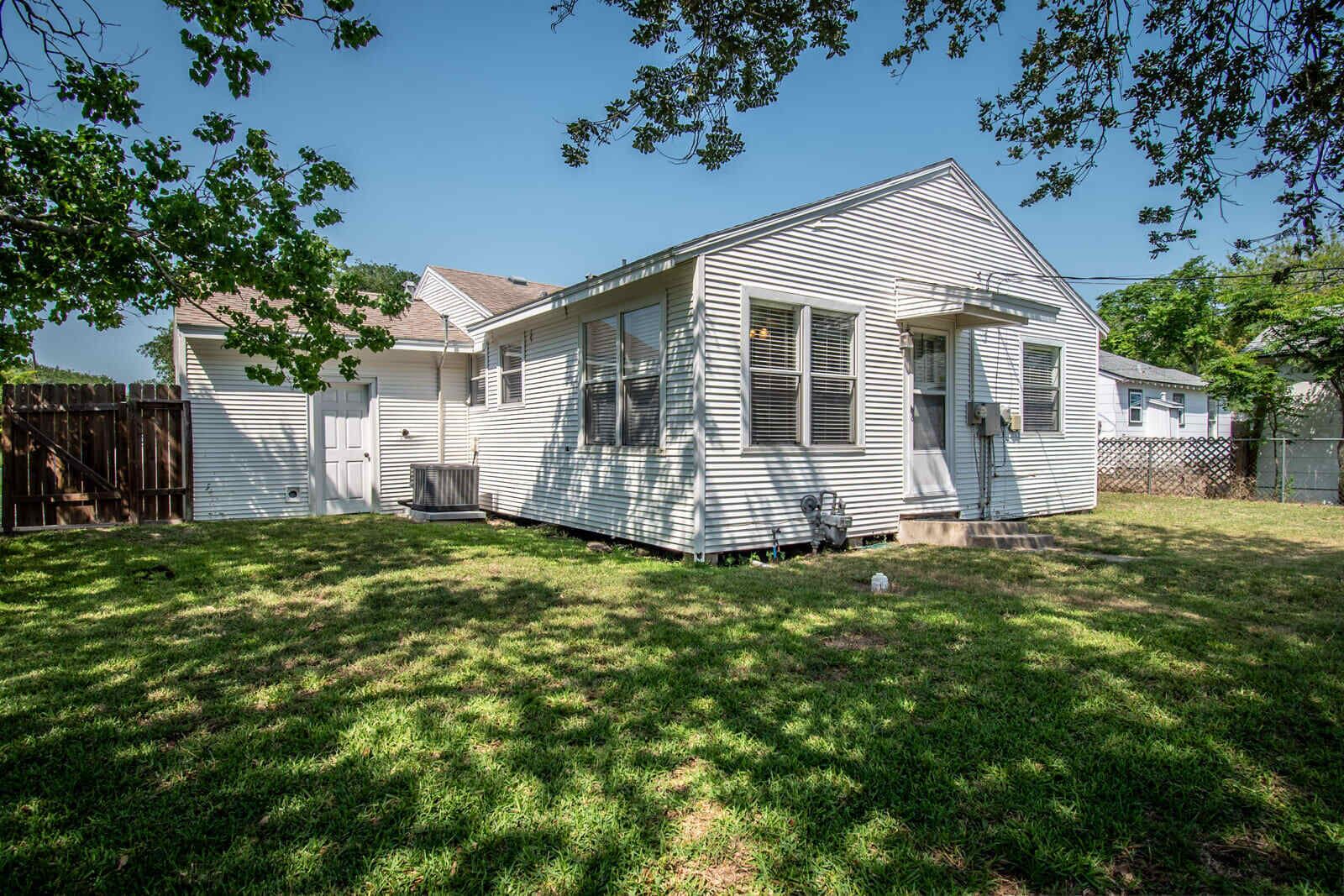A single-story house with a sloped roof, a front porch, and a fenced backyard.