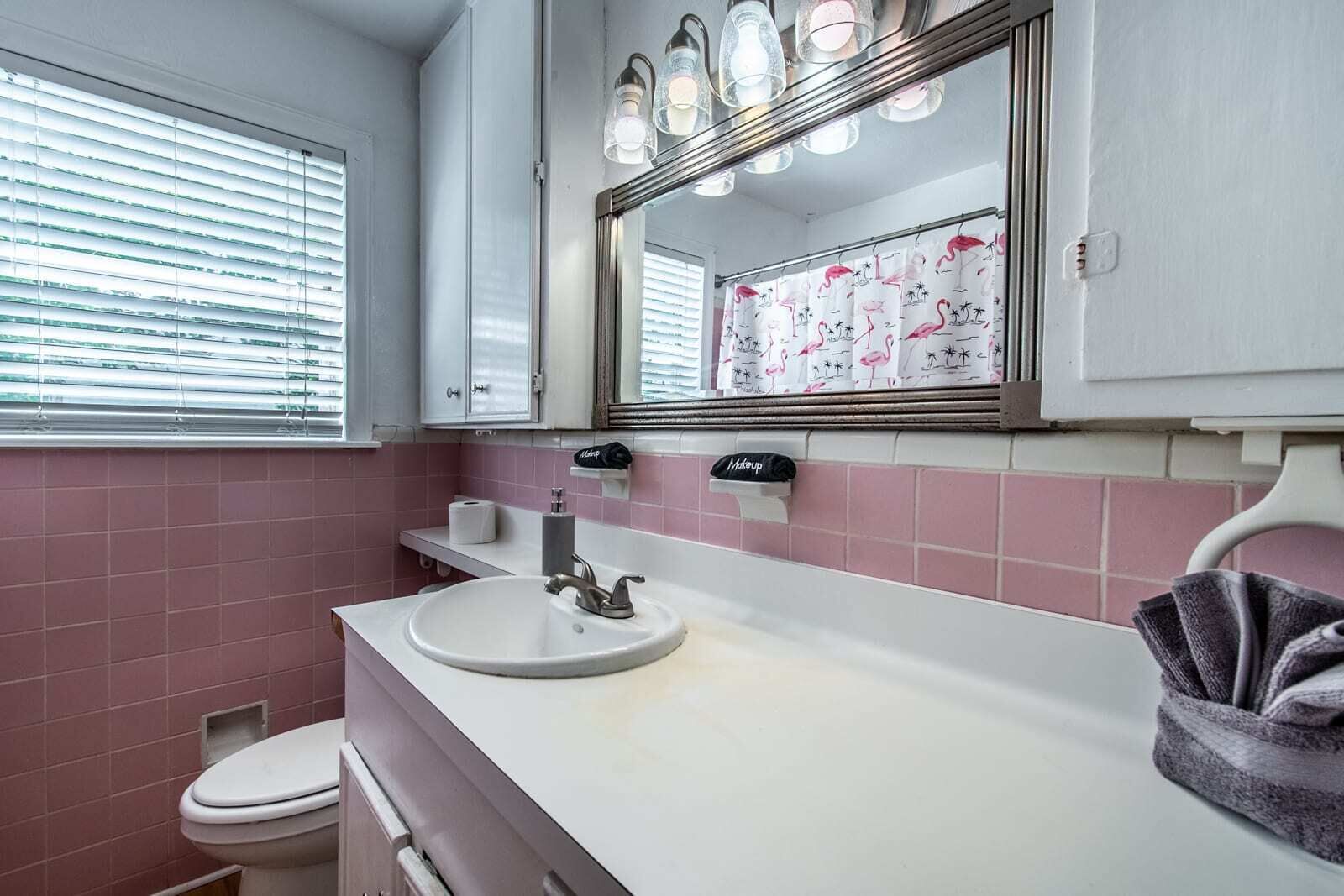 A bathroom with a white sink, pink tiles, a toilet, and a mirror with lights.