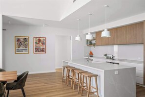 Une cuisine moderne avec un îlot central, des luminaires suspendus et des œuvres d’art encadrées accrochées au mur.