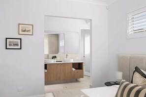 A modern bedroom with a bed, a nightstand, a bedside table, and a window with blinds. - Genoa House—Coastal Elegance at the Marina's Edge (Geographe)