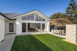 Une maison moderne dotée d’une grande porte vitrée donnant sur un espace intérieur, d’une pelouse bien entretenue et d’un patio aménagé avec du mobilier d’extérieur.