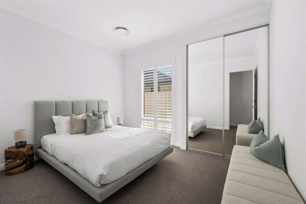 A modern bedroom with a large bed, a sofa, a mirror, and a sliding door leading to a bathroom.