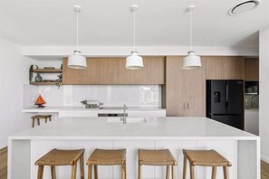 A modern kitchen with a large island, white cabinetry, and three pendant lights. - Genoa House—Coastal Elegance at the Marina's Edge (Geographe)