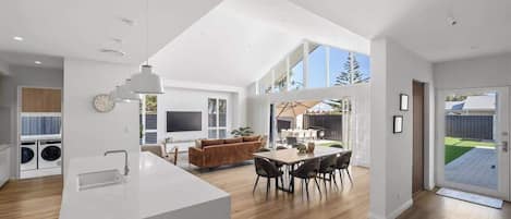 A modern kitchen with a central island, dining area with a table and chairs, and a living space with a sofa and TV.