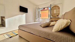 Ein Schlafzimmer mit Bett, Wandfernseher, Fenster mit freier Aussicht und einem dekorativen Wandbild.