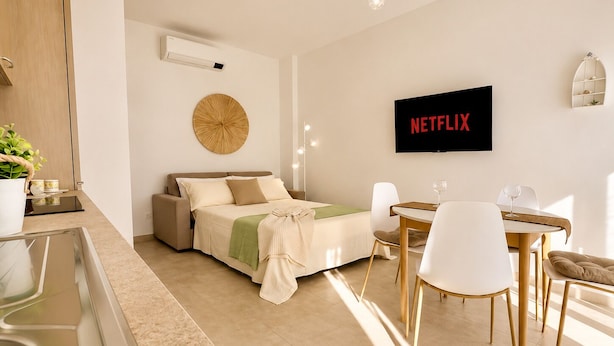 A modern bedroom with a bed, bedside table, and a wall-mounted TV displaying 'NETFLIX'. - 1-Bedroom Apt 30m from Sea | AC | Terrace | Bike Friendly + Box (Finale Ligure)