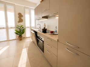 A modern kitchen with sliding doors, a sink, a stove, and a countertop with a kettle and a water bottle. - 1-Bedroom Apt 30m from Sea | AC | Terrace | Bike Friendly + Box (Finale Ligure)