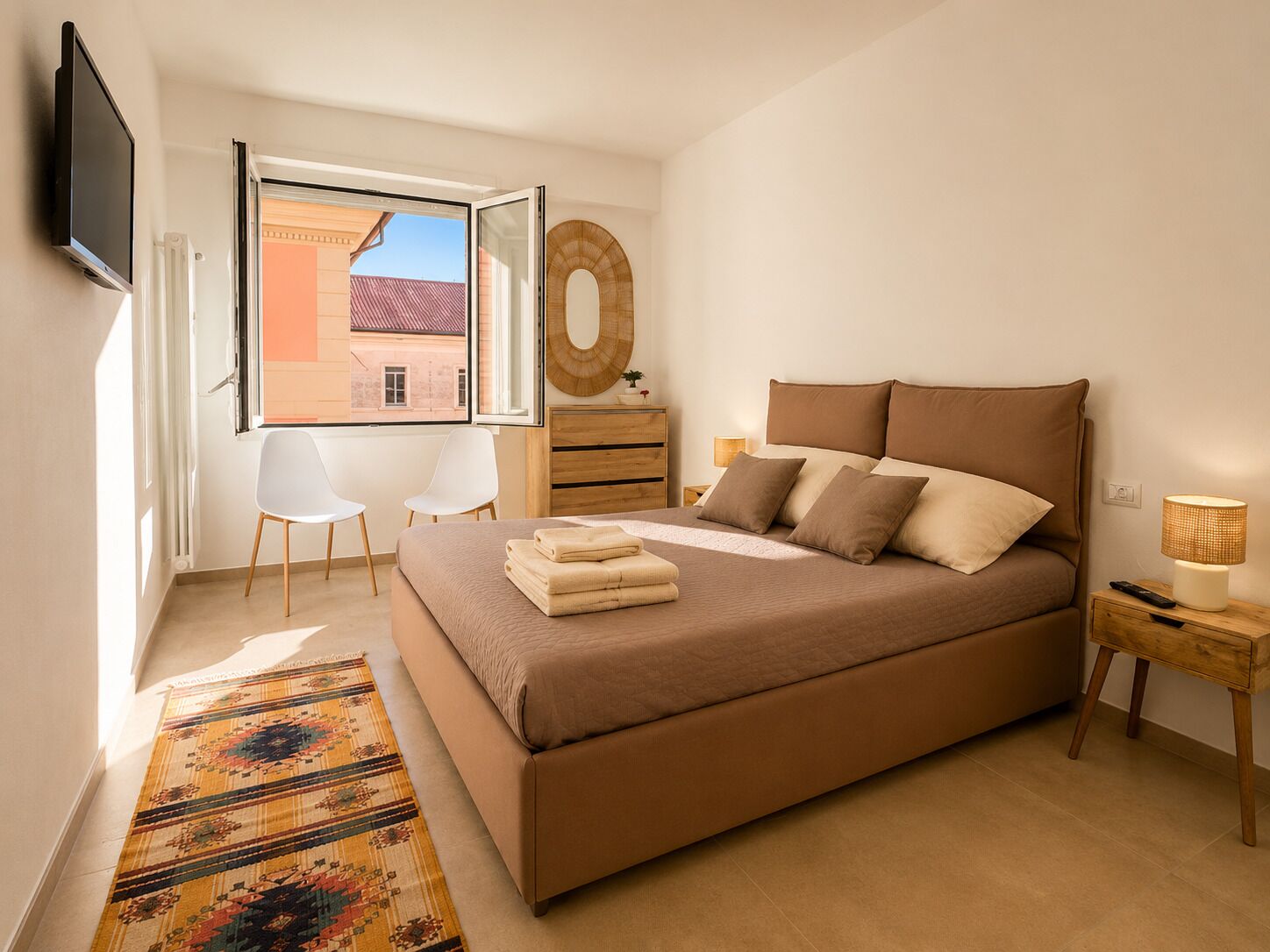 A bedroom with a bed, a TV, a window, a chair, a dresser, and a lamp.