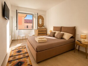 A bedroom with a bed, a TV, a window, a chair, a dresser, and a lamp.