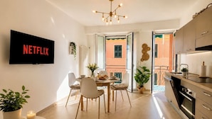A modern apartment with a dining area, kitchen, and a TV mounted on the wall. - 1-Bedroom Apt 30m from Sea | AC | Terrace | Bike Friendly + Box (Finale Ligure)