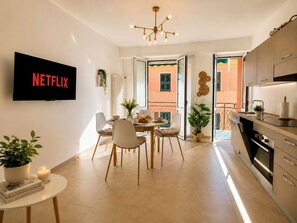 Moderni huoneisto, jossa on ruokailutila, keittiö ja seinälle asennettu televisio.