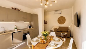A modern kitchen with a dining area, a flat-screen TV, and a round wall decoration. - 1-Bedroom Apt 30m from Sea | AC | Terrace | Bike Friendly + Box (Finale Ligure)