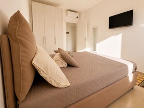 A bedroom with a bed, pillows, a television, and a wardrobe. - 1-Bedroom Apt 30m from Sea | AC | Terrace | Bike Friendly + Box (Finale Ligure)