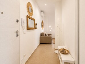 A hallway with a sofa, a wall-mounted mirror, and a small table with decorative items. - 1-Bedroom Apt 30m from Sea | AC | Terrace | Bike Friendly + Box (Finale Ligure)