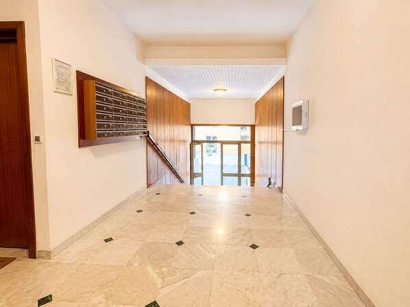 A hallway with a wooden staircase, a wall-mounted safe, and a door on the left.