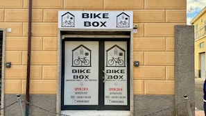 Ein Fahrradstellplatz mit Hinweisschild, das als Fahrradbox gekennzeichnet ist, geöffnet rund um die Uhr. Kontaktnummer und Webseite für weitere Informationen vorhanden.