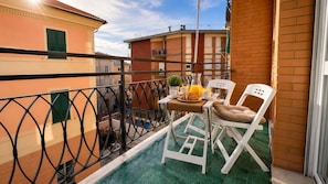 A balcony with a table set for breakfast, including croissants and orange juice, and a white chair. - 1-Bedroom Apt 30m from Sea | AC | Terrace | Bike Friendly + Box (Finale Ligure)