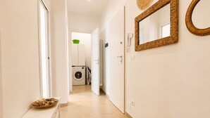 A hallway with a washing machine, a mirror, and a bench with a bowl of nuts. - 1-Bedroom Apt 30m from Sea | AC | Terrace | Bike Friendly + Box (Finale Ligure)