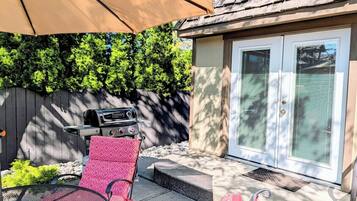 A patio area with a grill, a red chair, and a covered seating area.