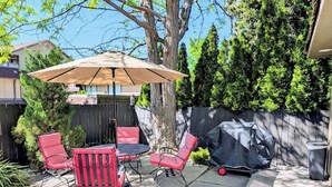 Une terrasse extérieure avec une table et des chaises, un parasol et un barbecue.
