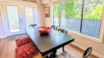 Un espace repas comprenant une longue table, des chaises, un lustre et une vue sur l’extérieur.