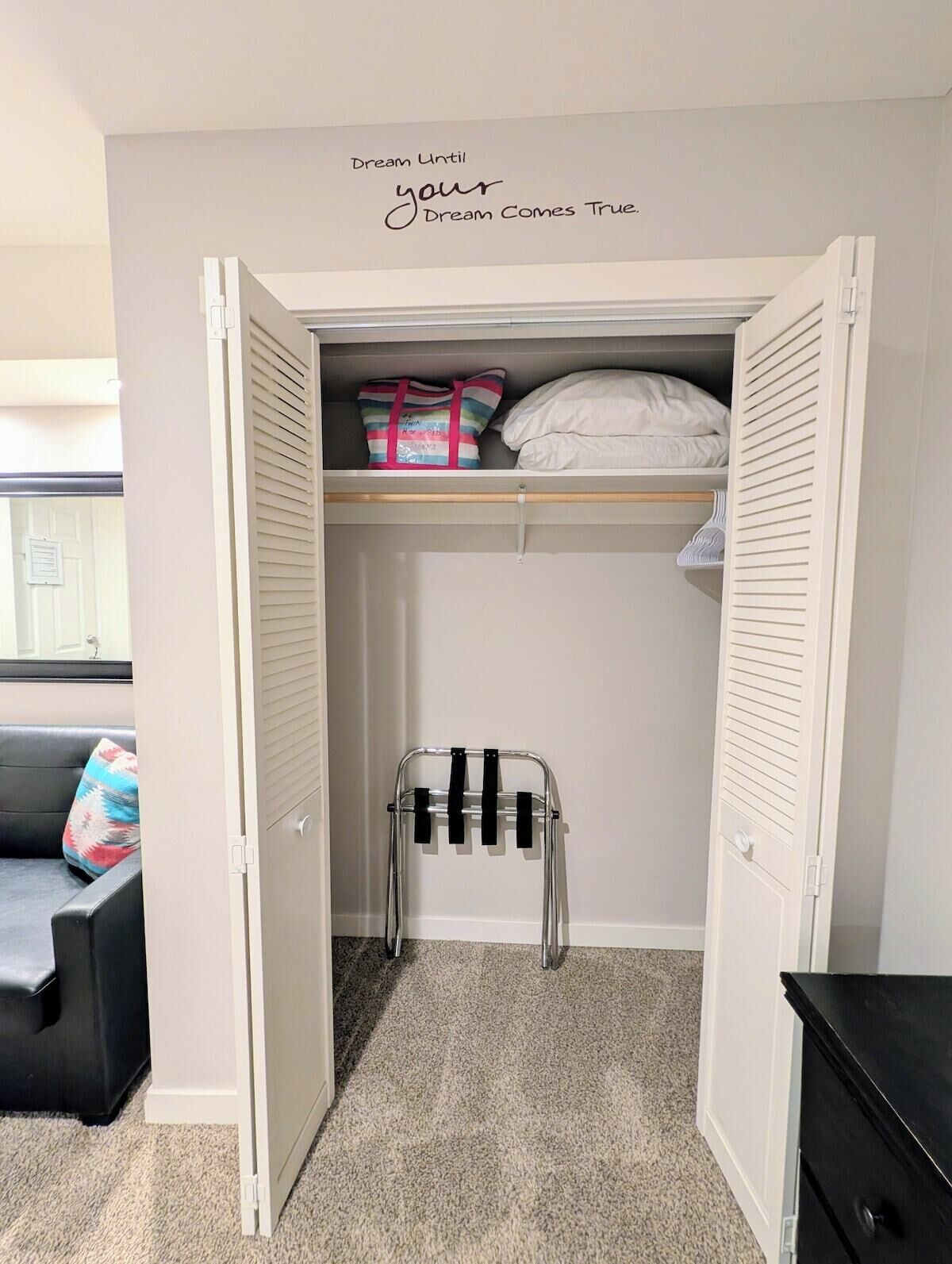 Un dressing avec un miroir, une tringle à vêtements et une étagère où sont pliés des vêtements.