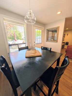 A dining area with a black table, woven placemat, and black chairs. - Patio Beach Retreat · Walk to Lake. 2 Bedroom, 1 Bath. Enjoy stair-free living, a full kitchen, private patio with grill, sun loungers, and easy access to Slidewaters, wineries, and downtown Chelan. (Chelan)