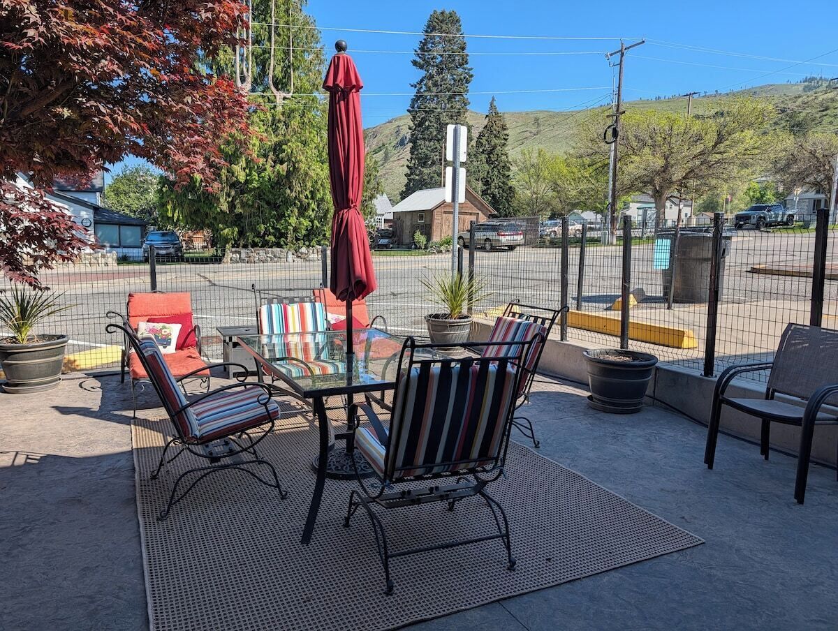 Un espace extérieur aménagé en terrasse, avec une table et des chaises, un parasol rouge et une zone délimitée par une clôture.
