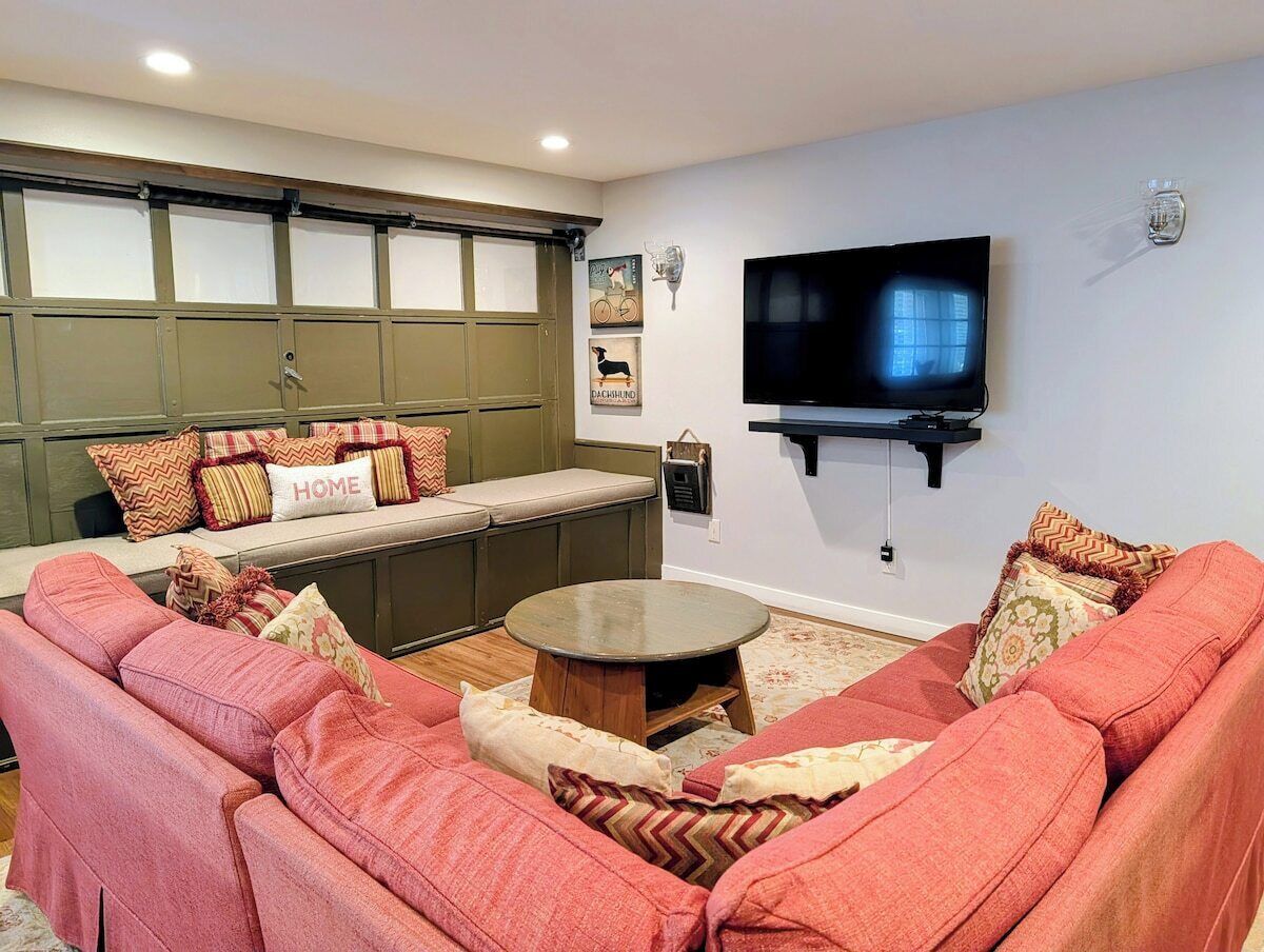 A living room with a sofa set, a coffee table, a bench with cushions, a mounted television, and wall-mounted artwork.